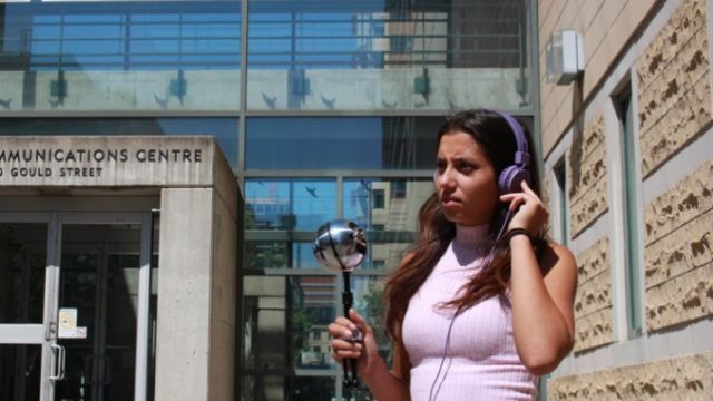 A student wearing headphones and holding a mic, stands outside the RCC. 