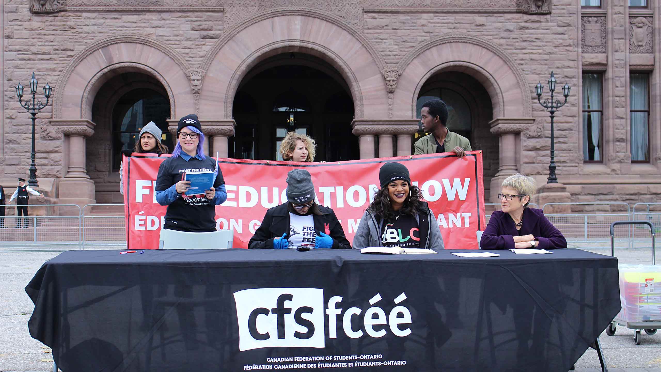 three CFS members sit at a table in front of city hall reading demands
