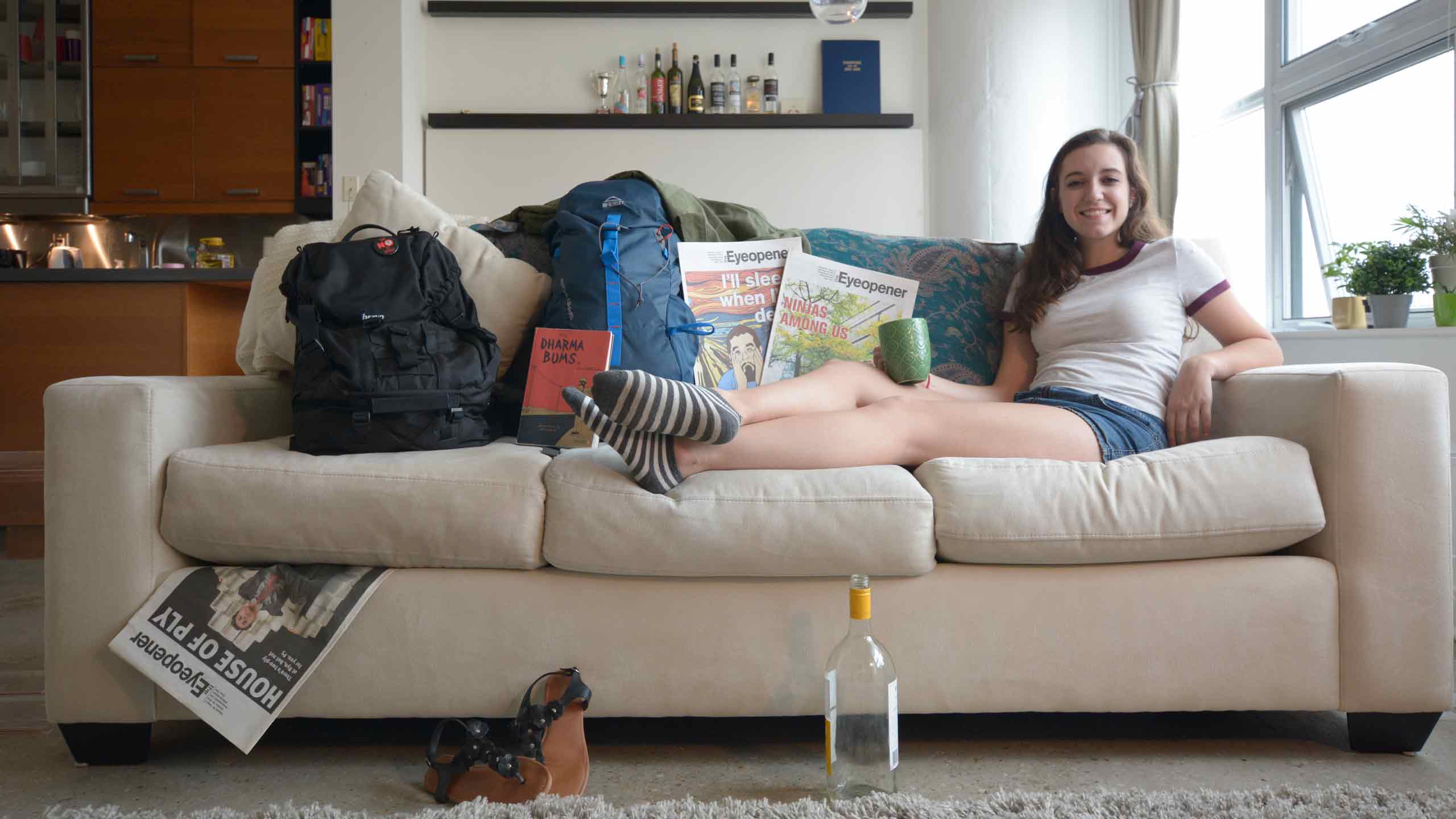 A girl laying on a couch surrounded by her travel items.