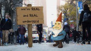 An elf stands on Gould Street next to a sign that reads: We're real and REAL underpaid!