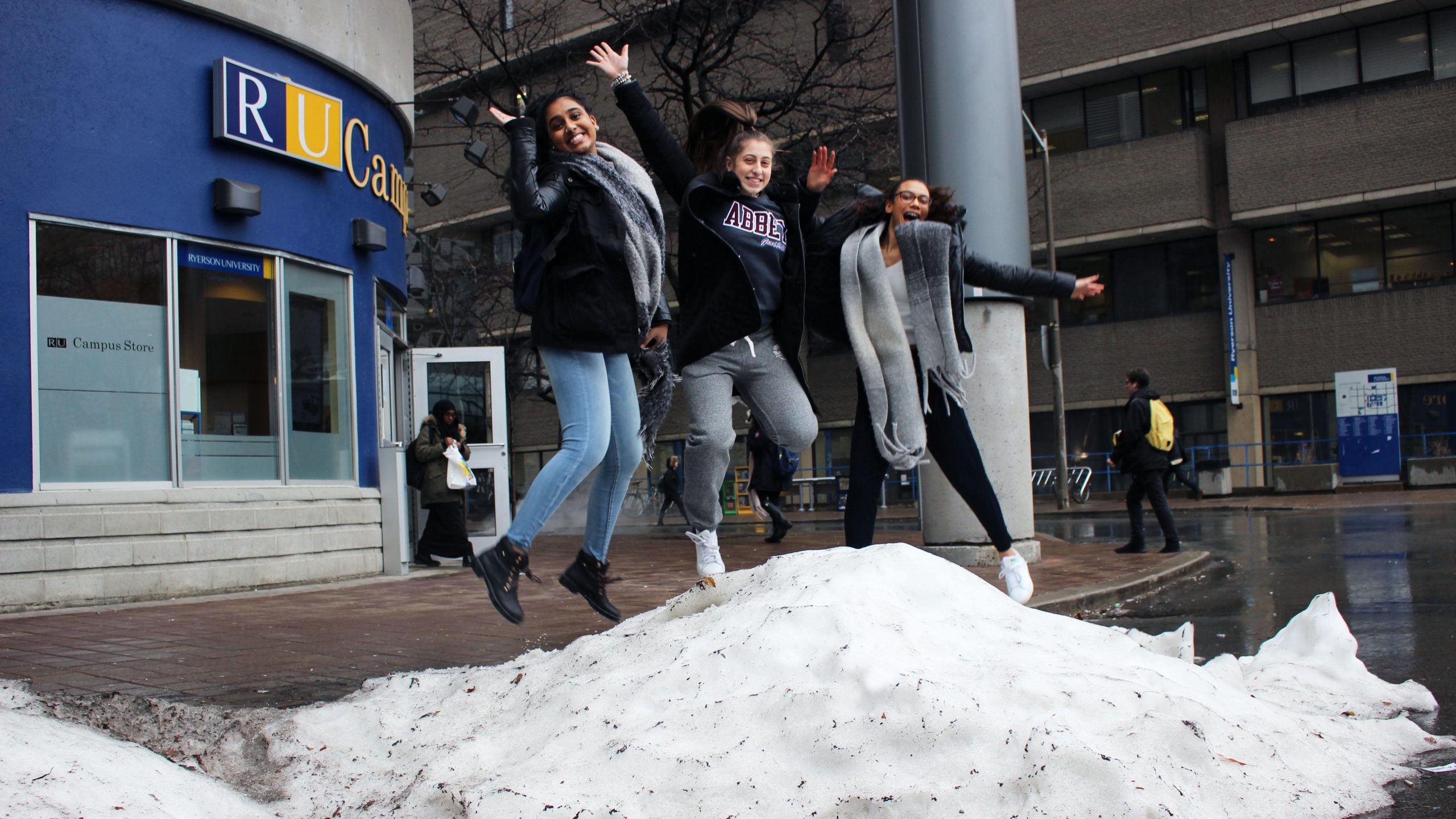 Three girls happily jump in a pile of snow on Gould Street.