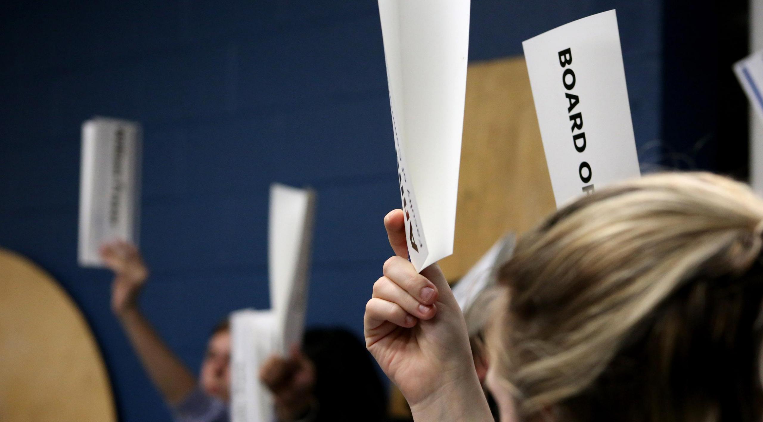 People holding up sheets of paper to vote in a Board of Directors meeting