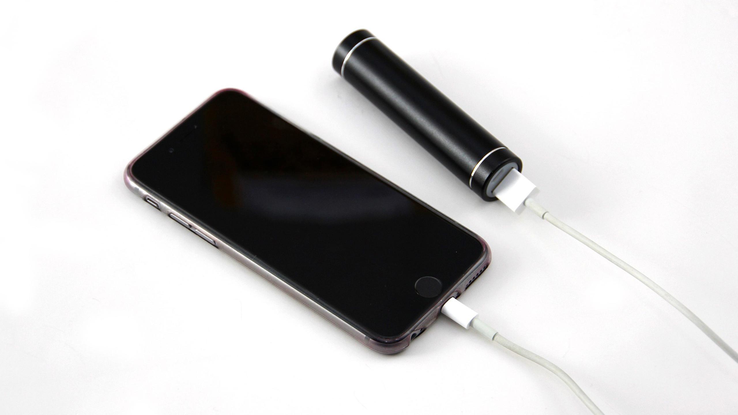 An iPhone and a portable charger sit side by side. Both are connected to charging cables. 