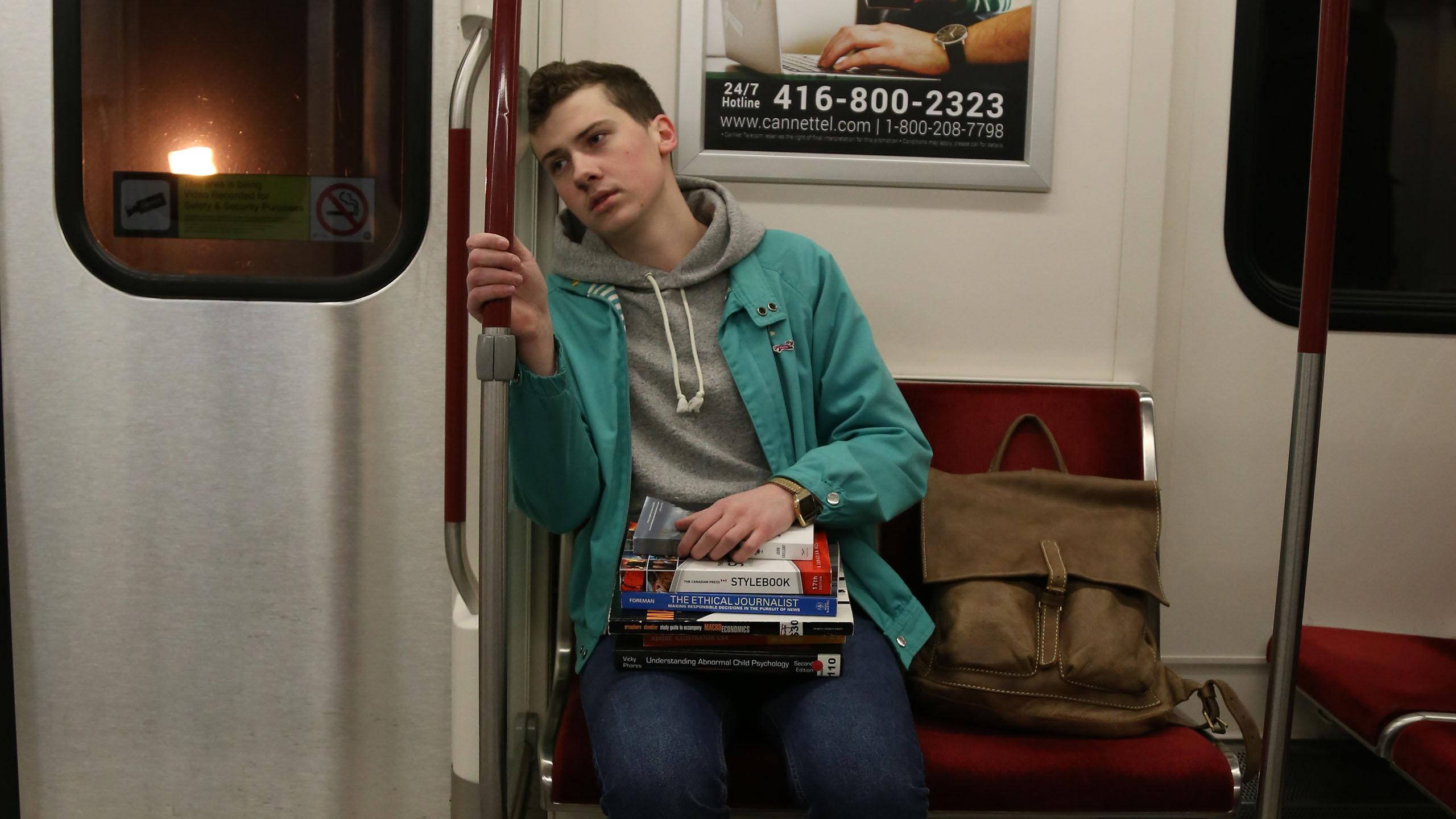 A student commuter sits in a subway car, looking exhausted