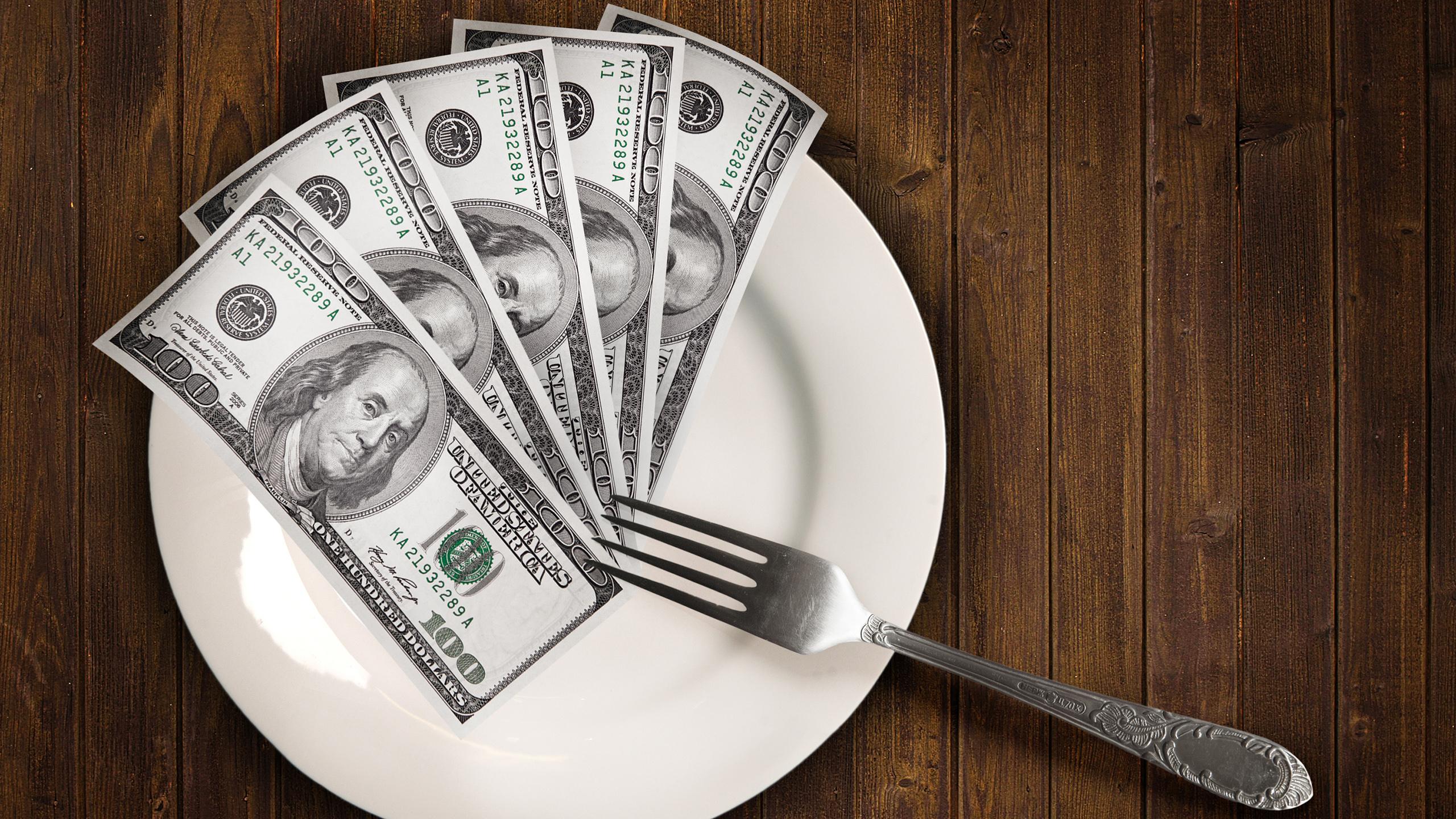 A stack of money sits on a dinner plate with a fork.