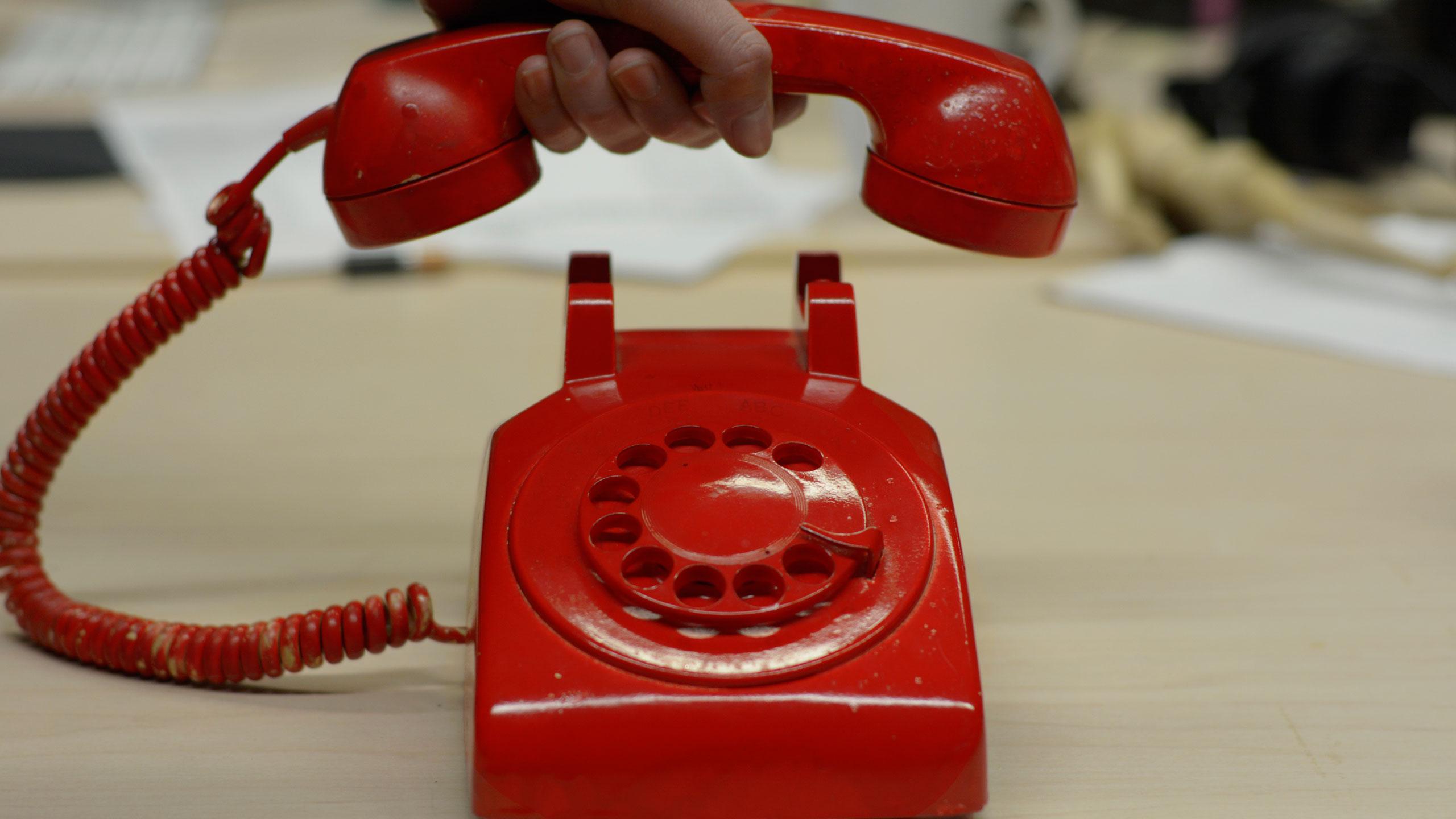 A red old style phone with a chord and dial.