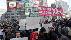 Protestors march down the streets at Yonge and Dundas. A sign that reads, "Refugees Welcome" is held