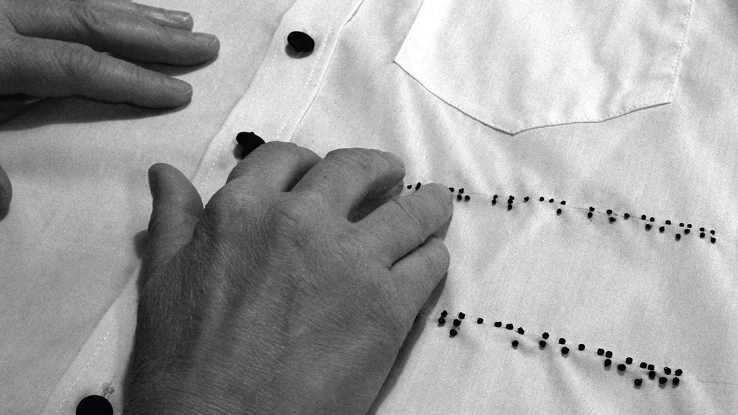 Hands reading braille on the front of a collared shirt