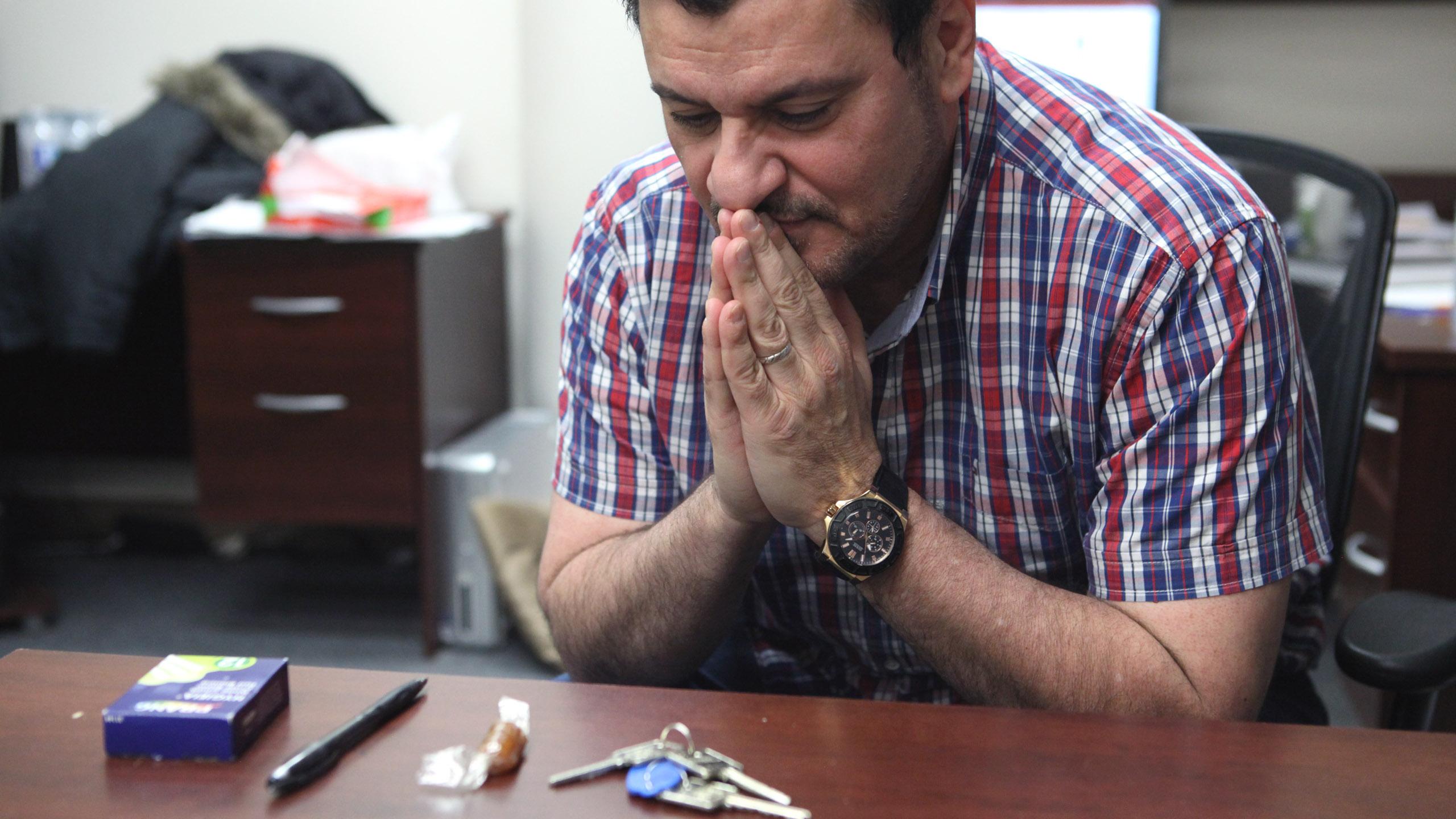 Dr.Majed, hands folded in prayer towards his tools of teaching. Keys, a candy, a pen and a box of staples.
