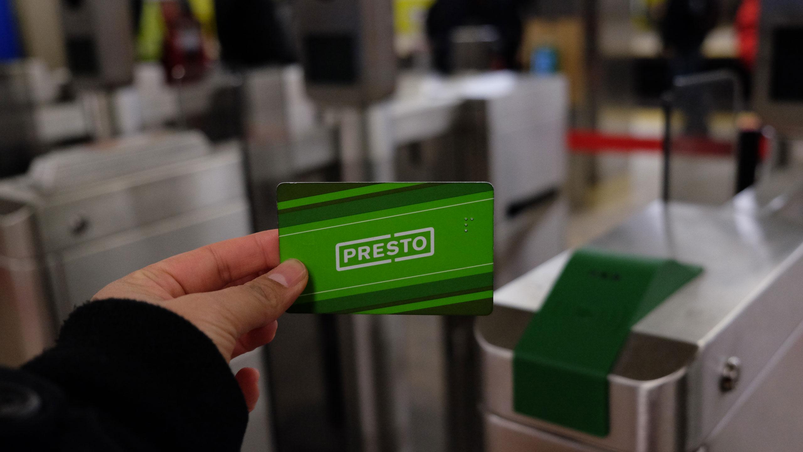 An arm holds a Presto card up in front of a fare gate