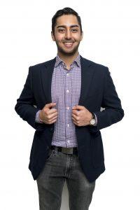 Faruqi stands in front of a white backdrop, hands on the front of his jacket.