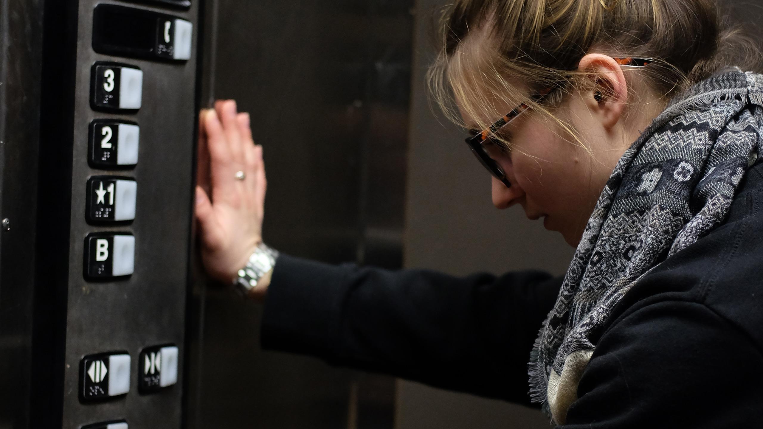 A student stands with their hand pressed against the side of an elevator, looking sadly at the buttons.