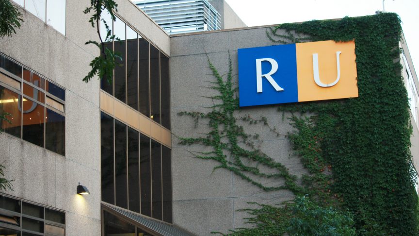 A vine covered building with the letters RU on it, the R in a blue square and the U in a yellow square