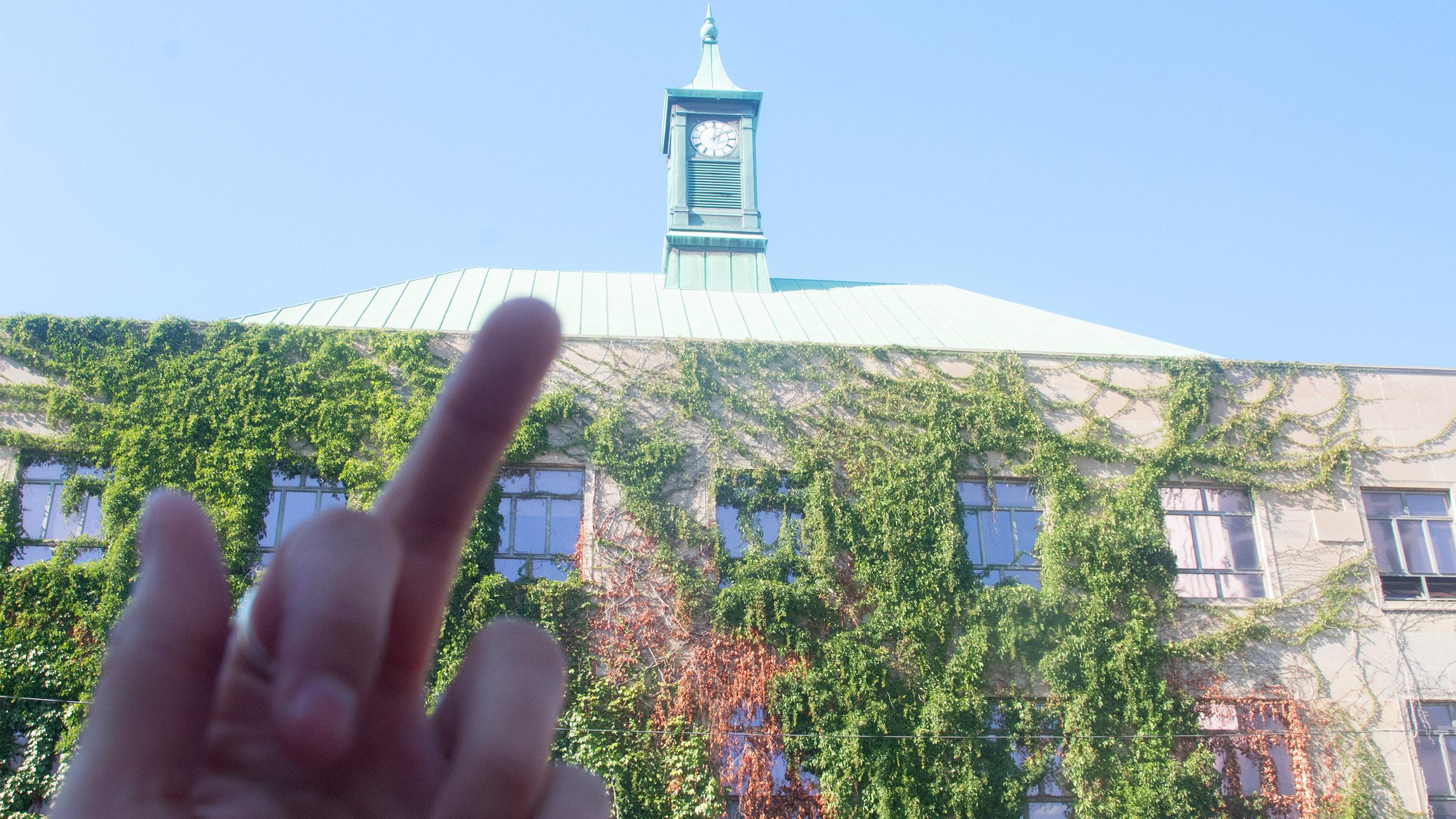 A photo of a student giving the middle finger to the broken clock on the outside of Kerr Hall