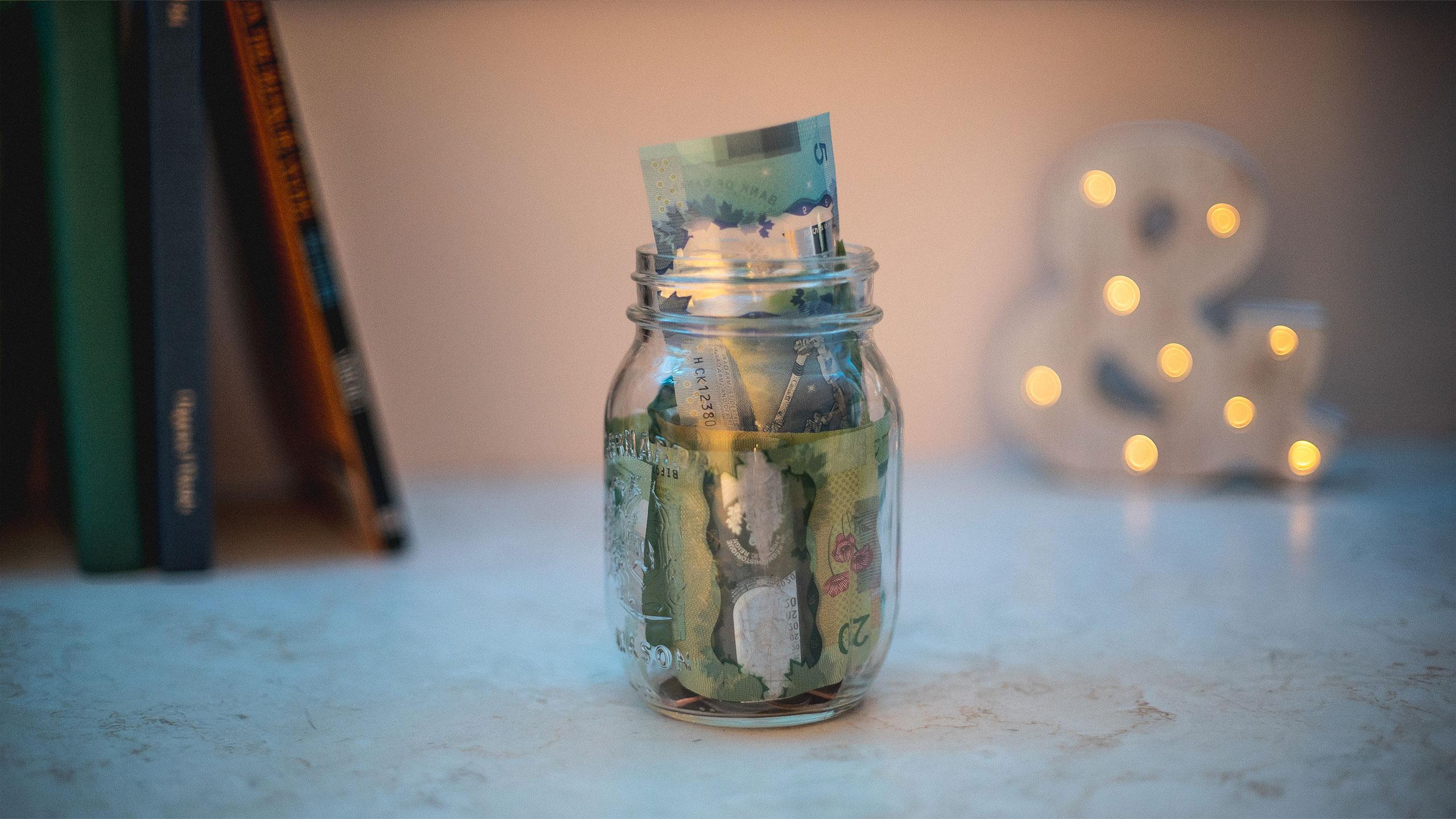 A savings jar brimming with $20 and $5 bills