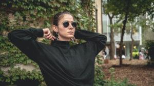 A photo of a student in a black turtleneck and sunglasses pulling on the collar of their sweater