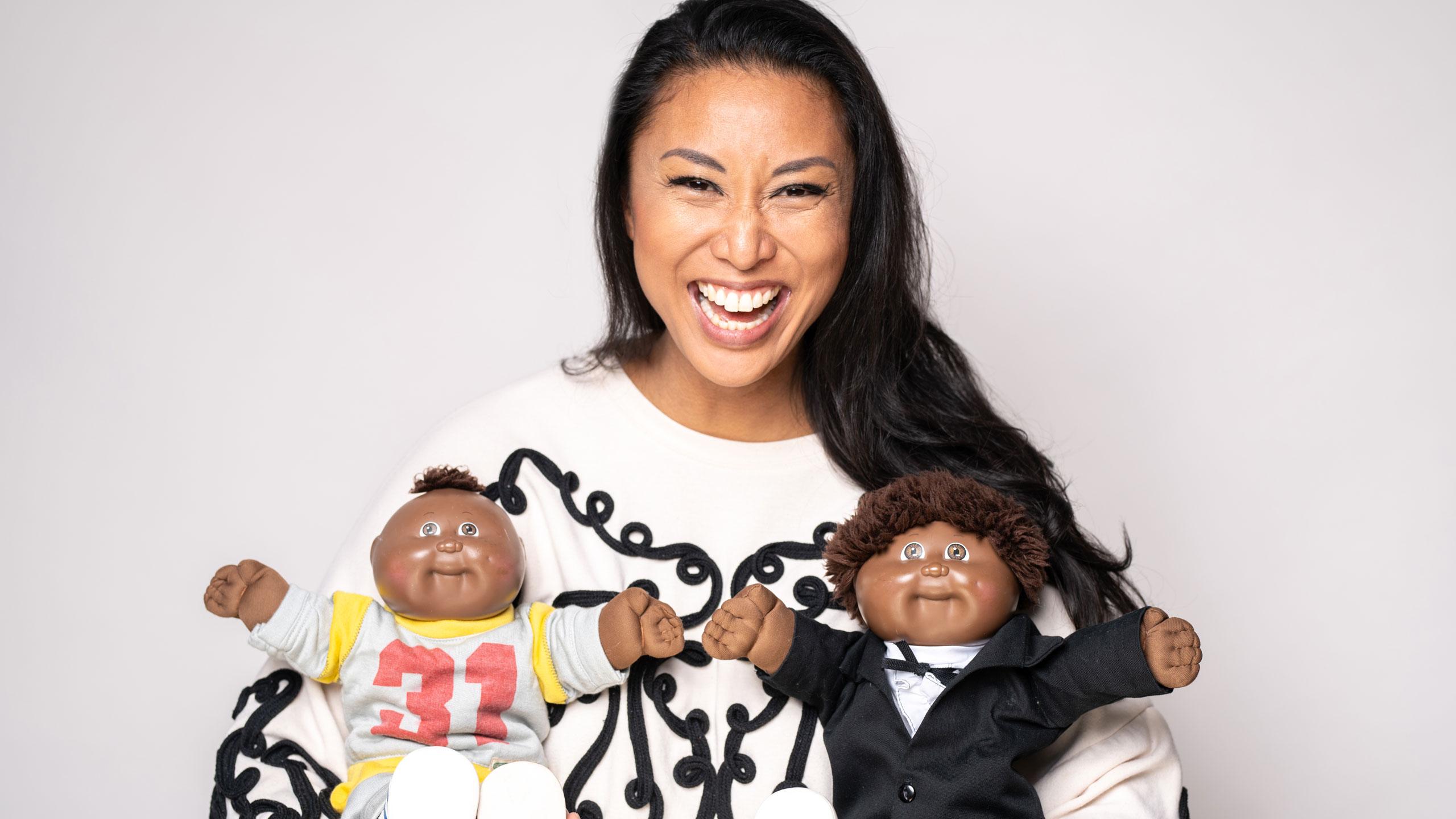 Author Catherine Hernandez holding two Black, male dolls.