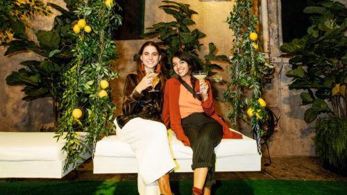 Editors Sarah and Andrea pose on a white bench hanging from a set of vines with lemons