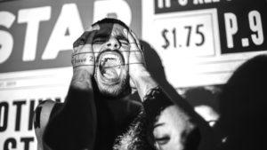 A person with newspaper headlines projected onto their face in black and white as they scream with their hands held on their face
