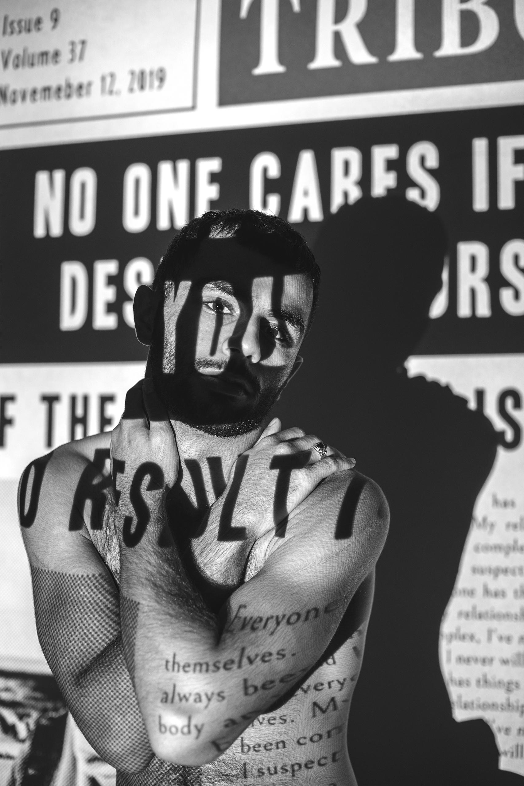 A black and white photo of a topless man with newspaper projection on his body that say terrible things