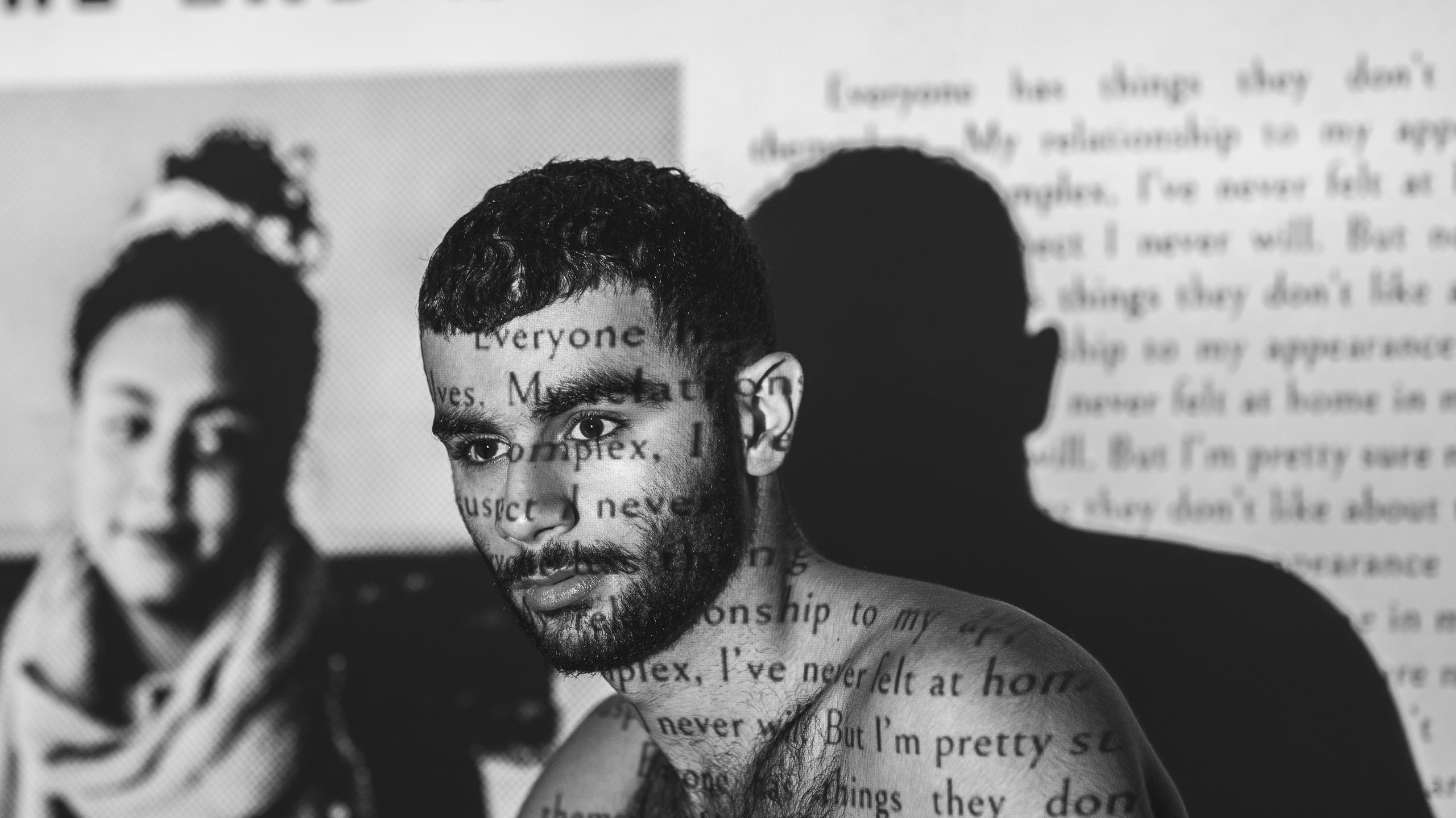 A black and white photo of a topless man with newspaper projection on his body that say terrible things