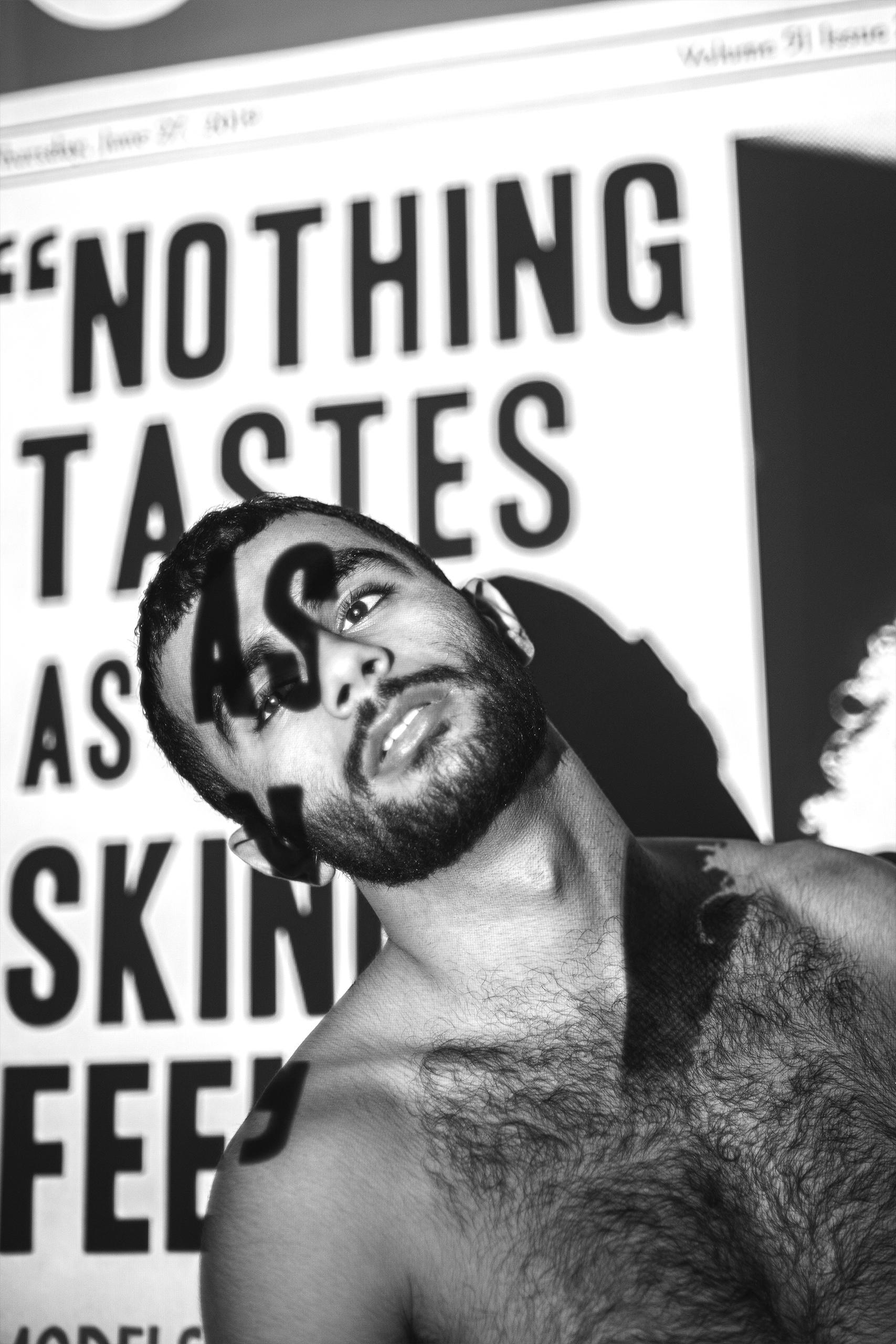 A black and white photo of a topless man with newspaper projection on his body that say terrible things