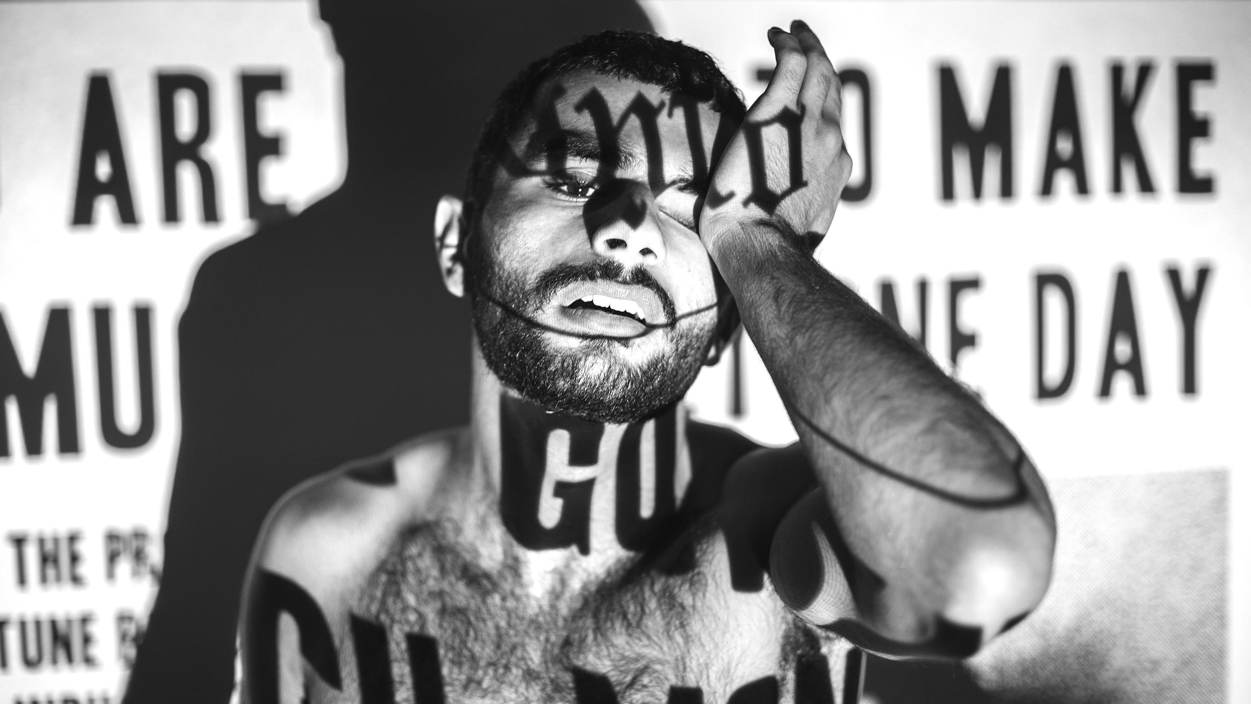 A black and white photo of a topless man with newspaper projection on his body that say terrible things