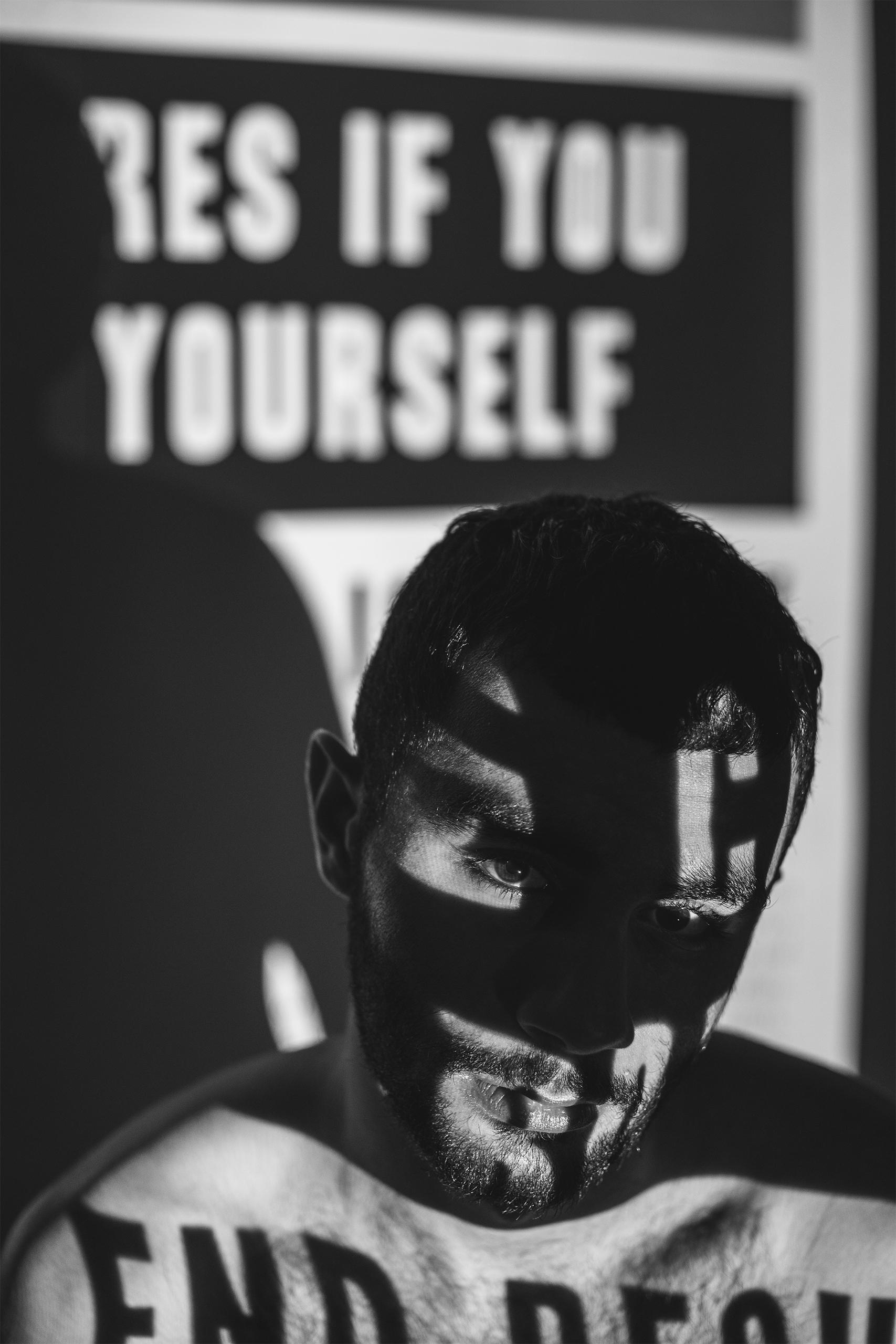 A black and white photo of a topless man with newspaper projection on his body that say terrible things