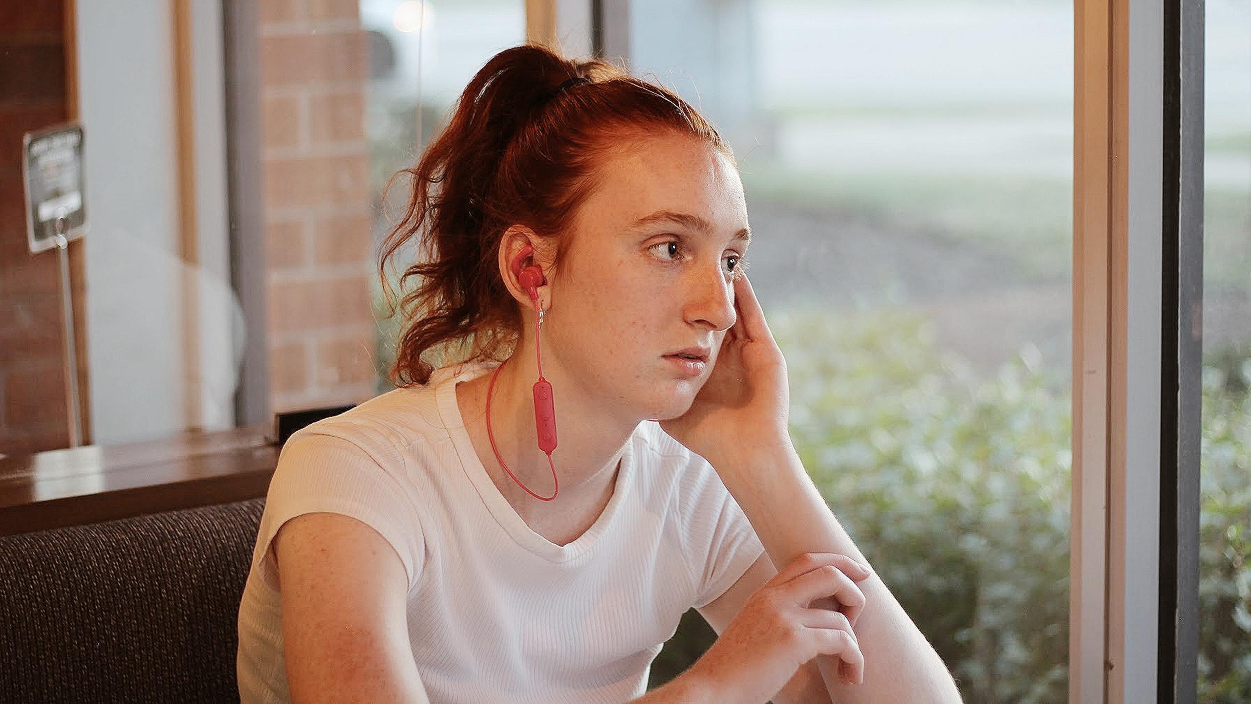 Picture of young woman staring out a window with headphones in.