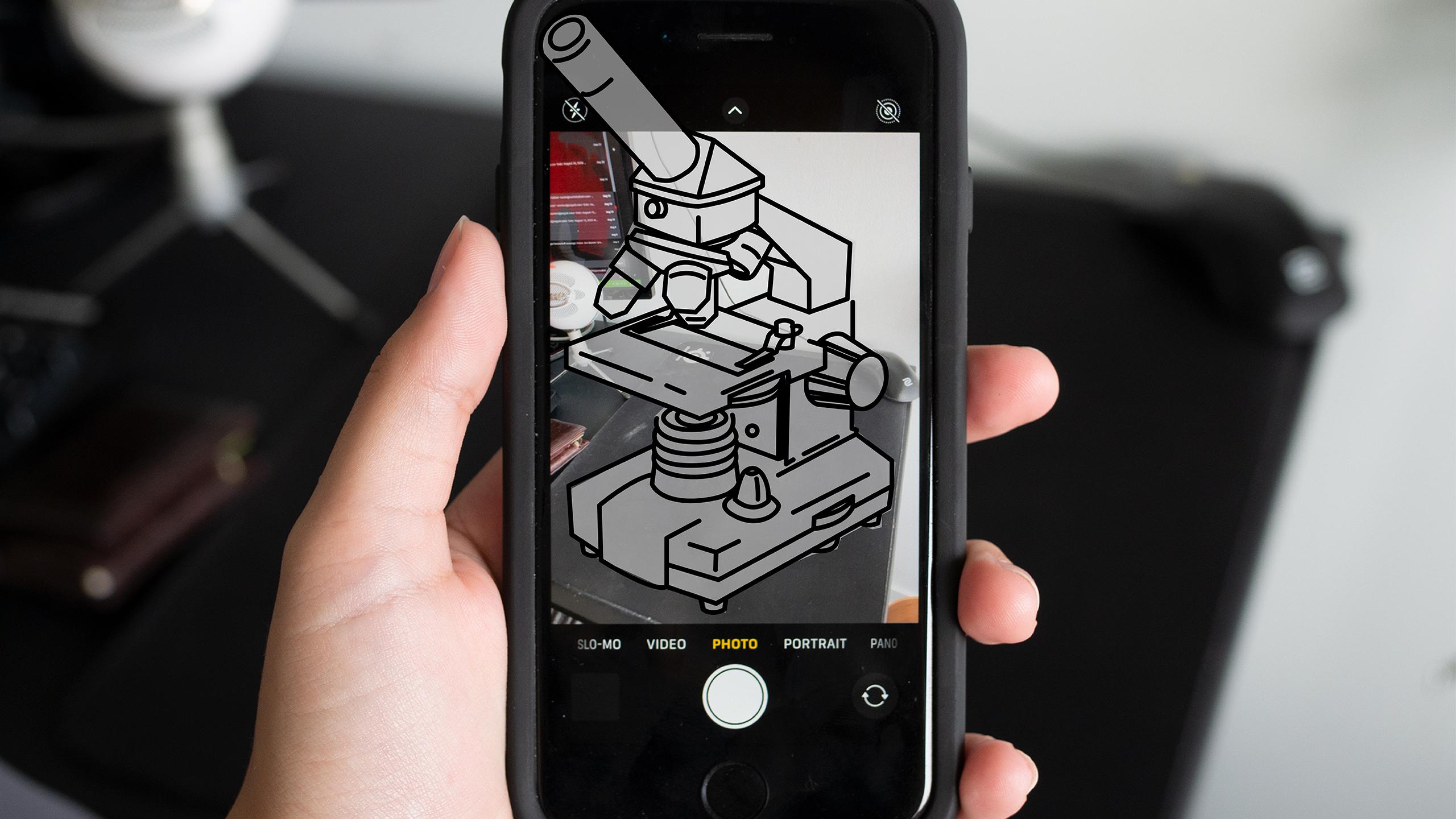 A photo of an iPhone taking a picture of a desk. On the screen, there is an illustration of a microscope as if the phone is using augmented reality technology.