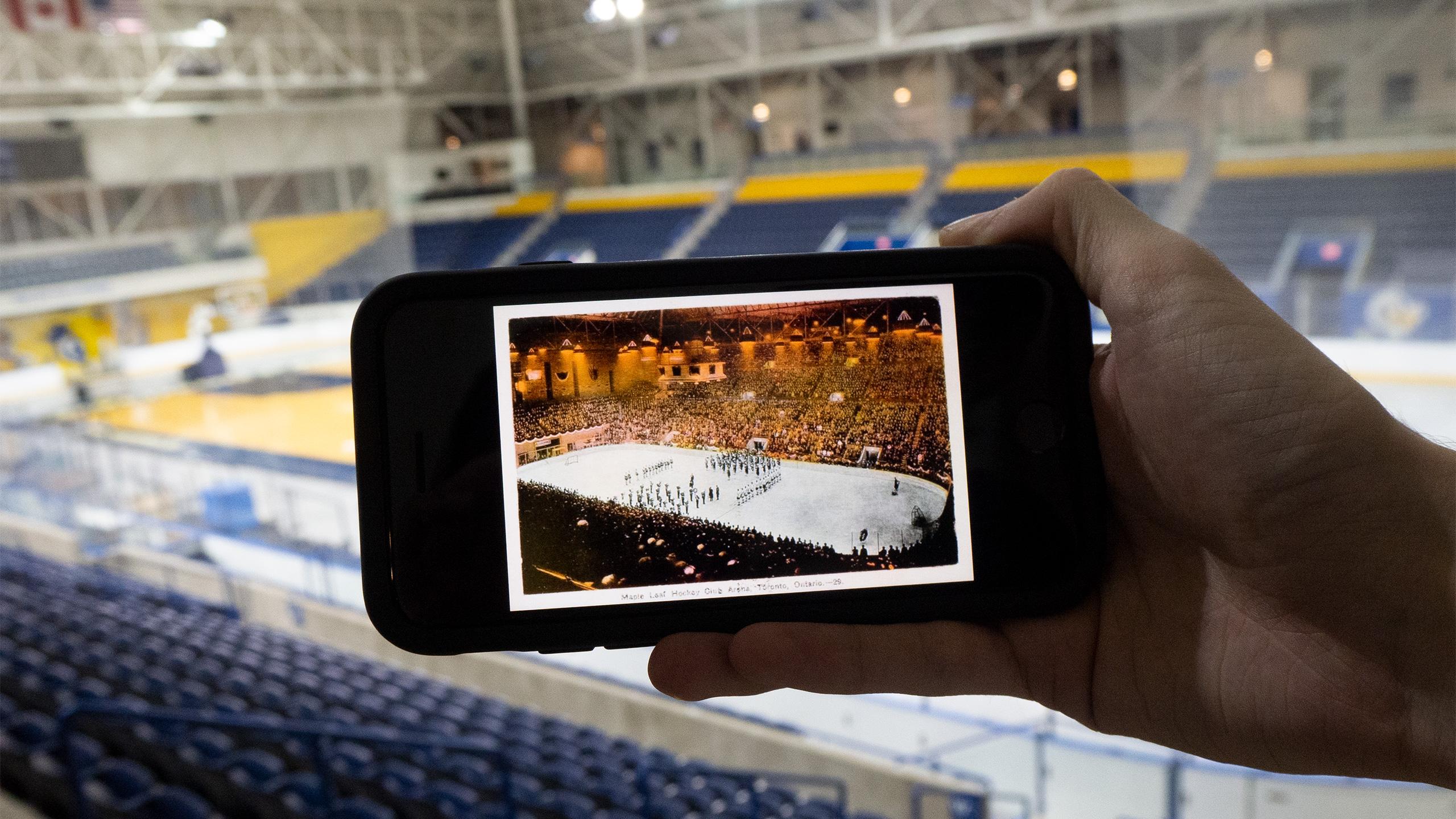 Someone holding up a picture of the old Maple Leaf Gardens arena in front of the current MAC arena.