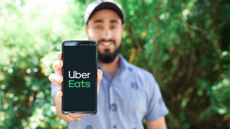 A smiling man holding a phone with the Uber Eats app.