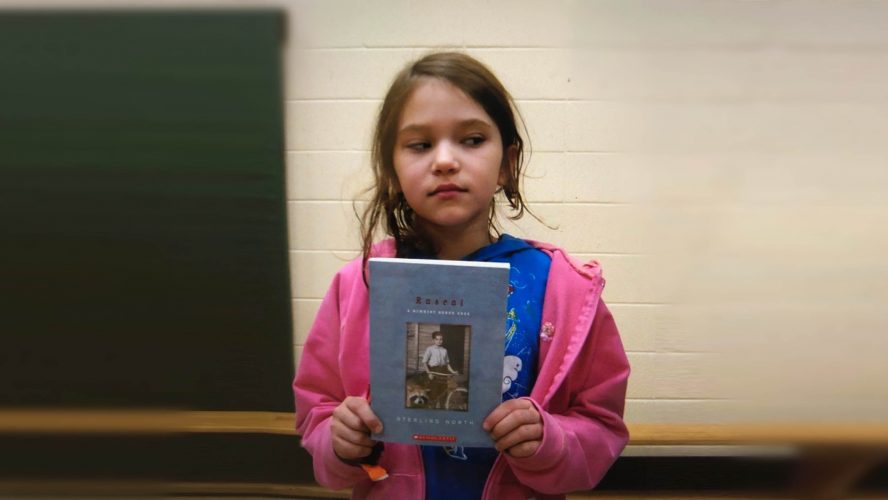 Young girl holds book wearing a pink sweater