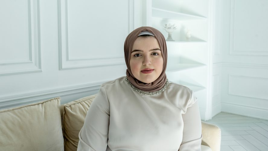 Mariam on a beige couch with a brown hijab and a stern look.