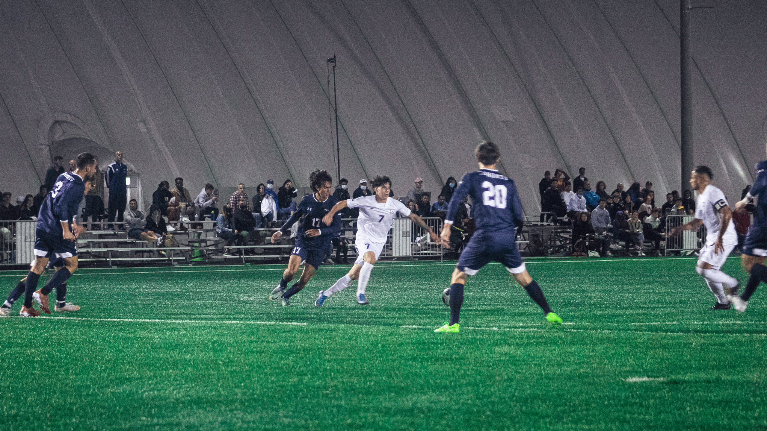 A rams men's soccer player in a white jersey is swarmed by a group of U of T defenders wearing navy blue uniforms