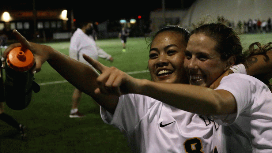 Two women smile and celebrate after winning a soccer game