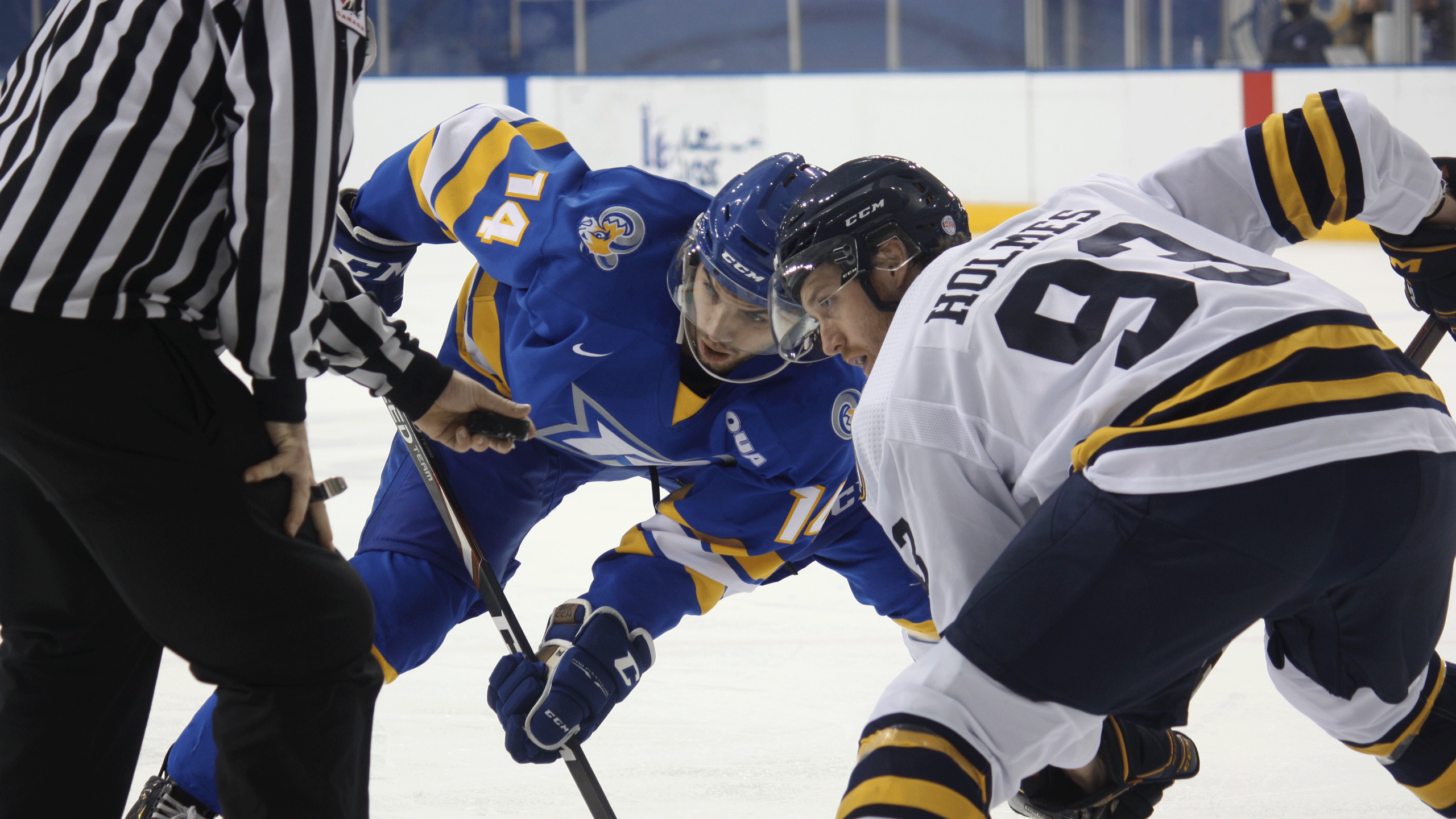 A Rams men's hockey player in a blue jersey lines up against his opponent