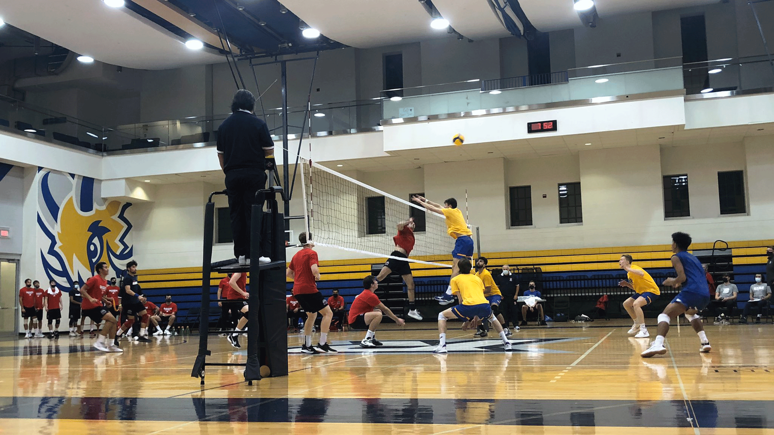 A Rams men's volleyball player in a yellow jersey goes up to the net to play the ball