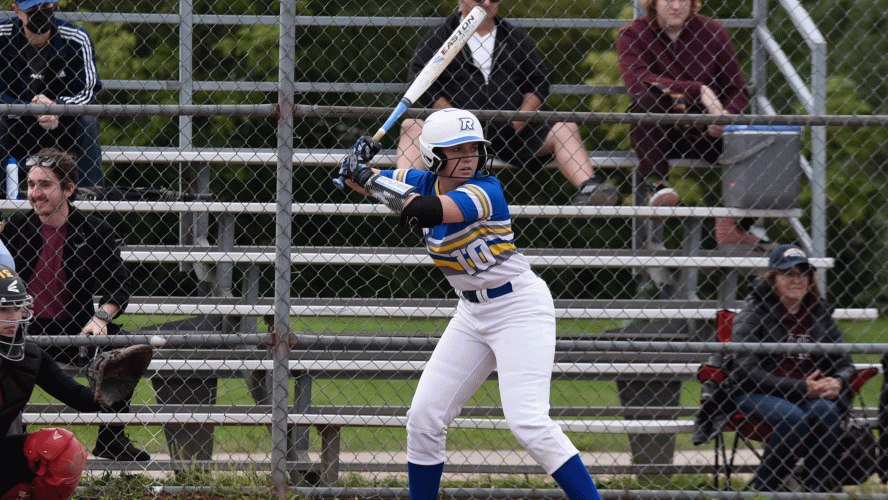 A Rams women's fastpitch player in a blue jersey awaits a pitch