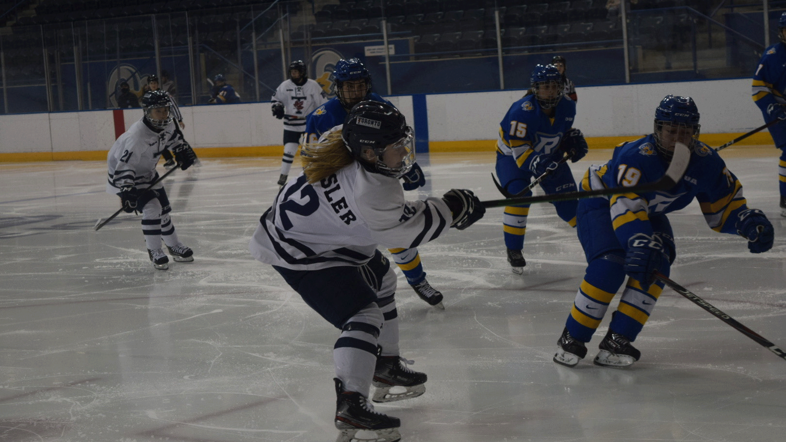 A U of T skater in a white jersey is closely defend by Rams players in blue jerseys