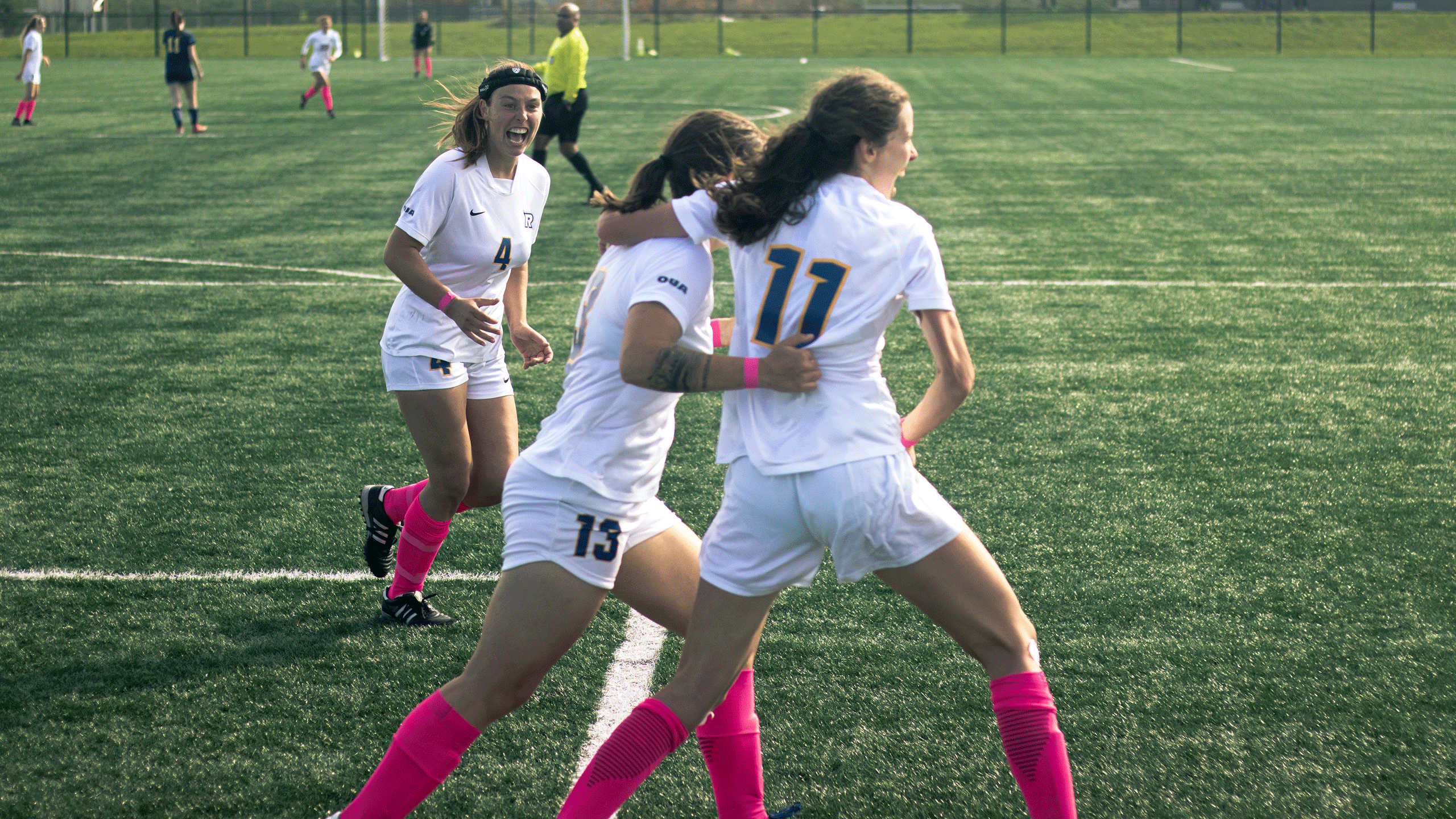 The Rams women's soccer team in white jerseys and pink socks celebrate after scoring a goal