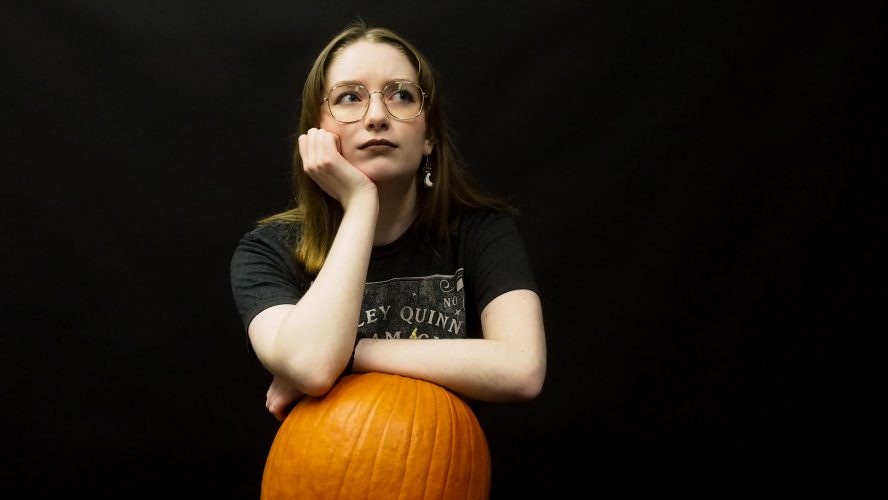 A student leaning on a pumpkin looking pensive