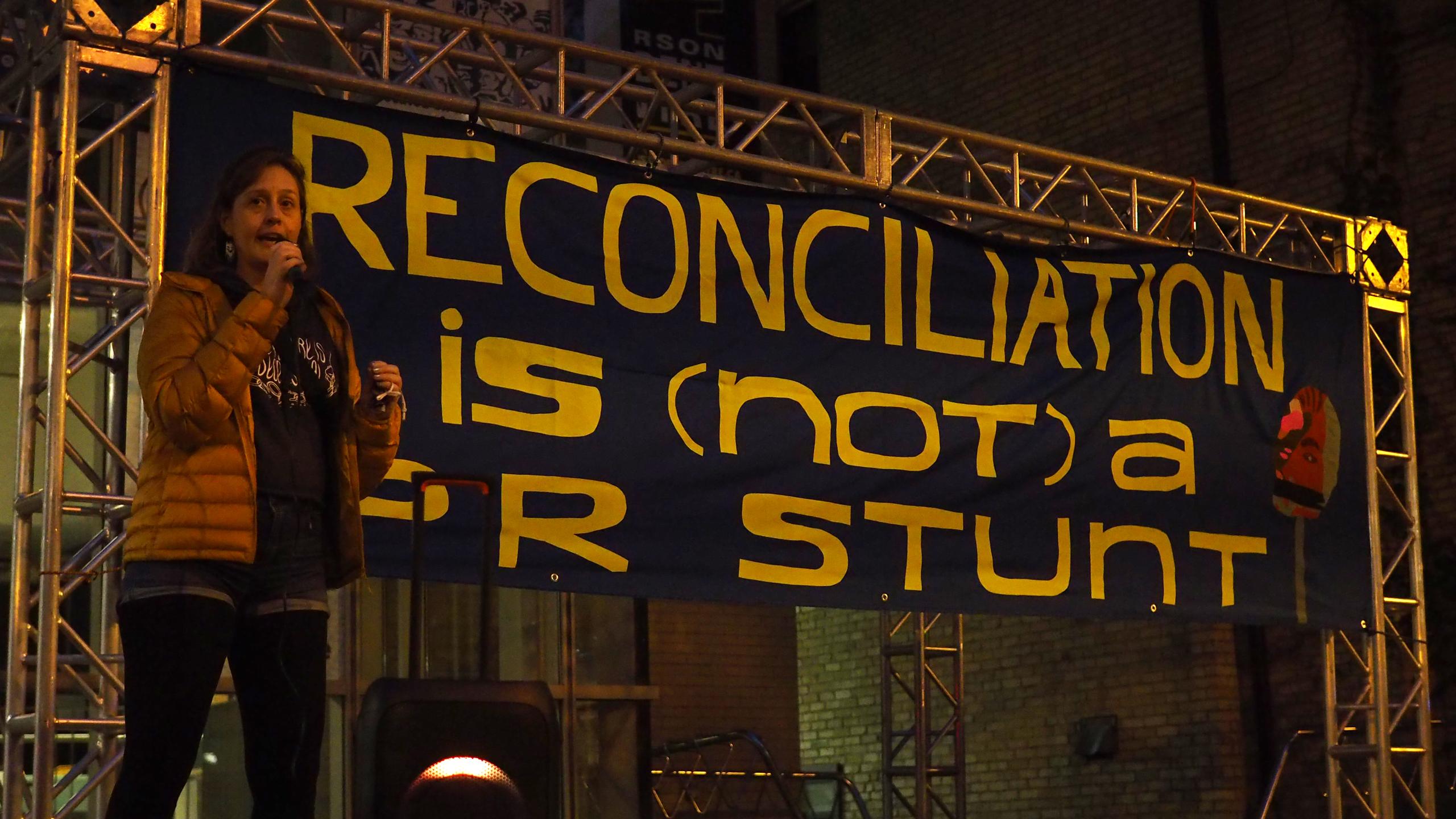 Miranda Black speaks at a rally calling for more Indigenous representation on Ryerson University's renaming advisory committee on Oct. 6, 2021. A large banner behind black reads: "Reconciliation is (not) a PR stunt."