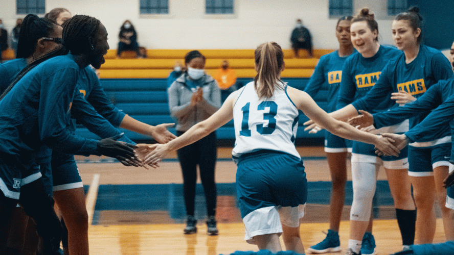 A woman in a white basketball jersey high-fives her teammates before the game