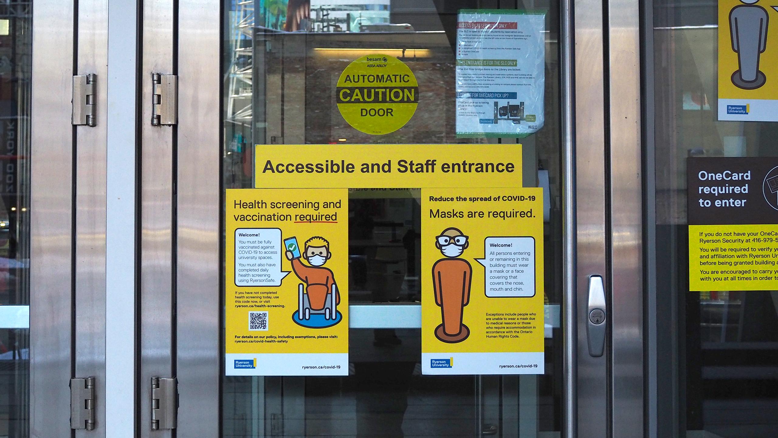 Signs on a door that say health screening and vaccination required and masks are required