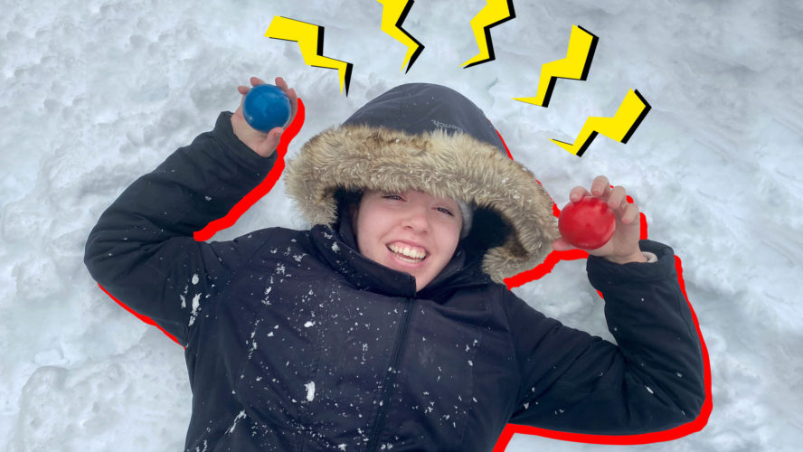 A girl smiling lying in the snow holding stress balls