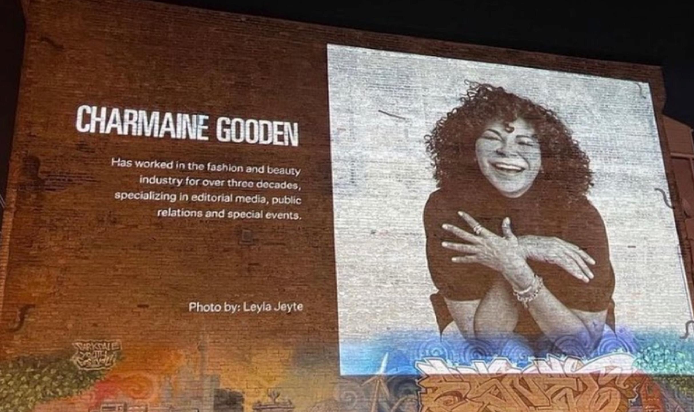 a projected image of a slide. To the left the name "Charmine Gooden" to the right a smiling and happy photo of her