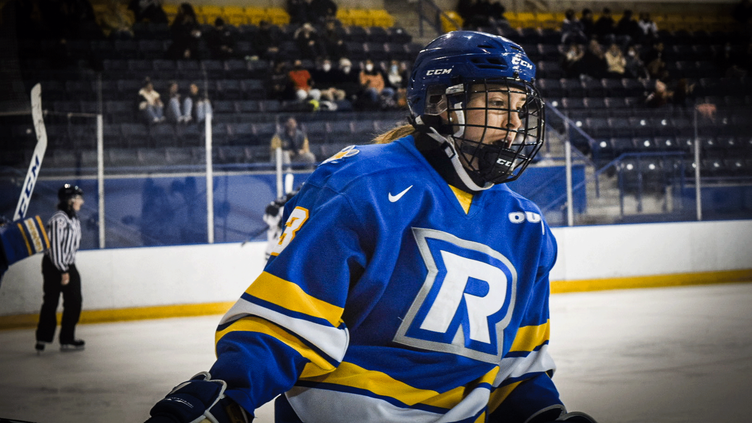 A Rams women's hockey player in a blue jersey skates by the glass