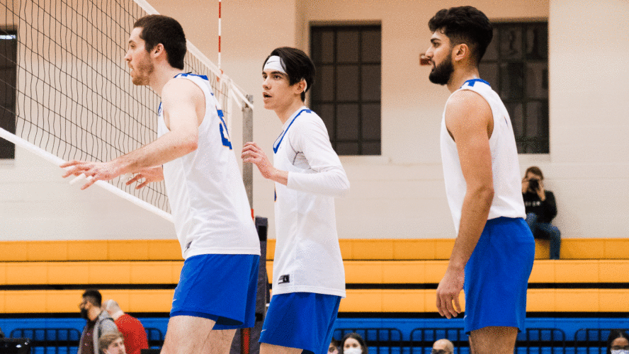 The Rams men's volleyball team in white jerseys guard the net