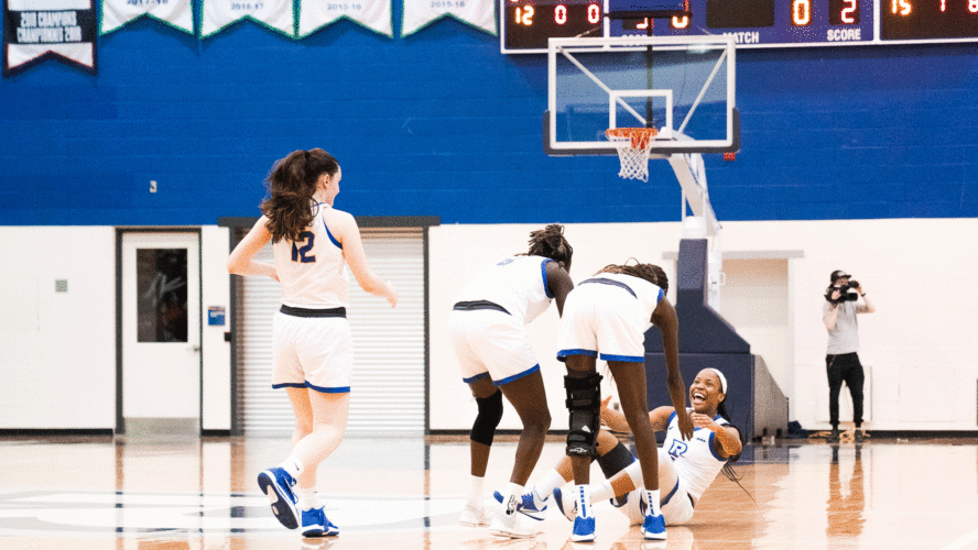 The Rams women's basketball team in white jerseys help up a teammate